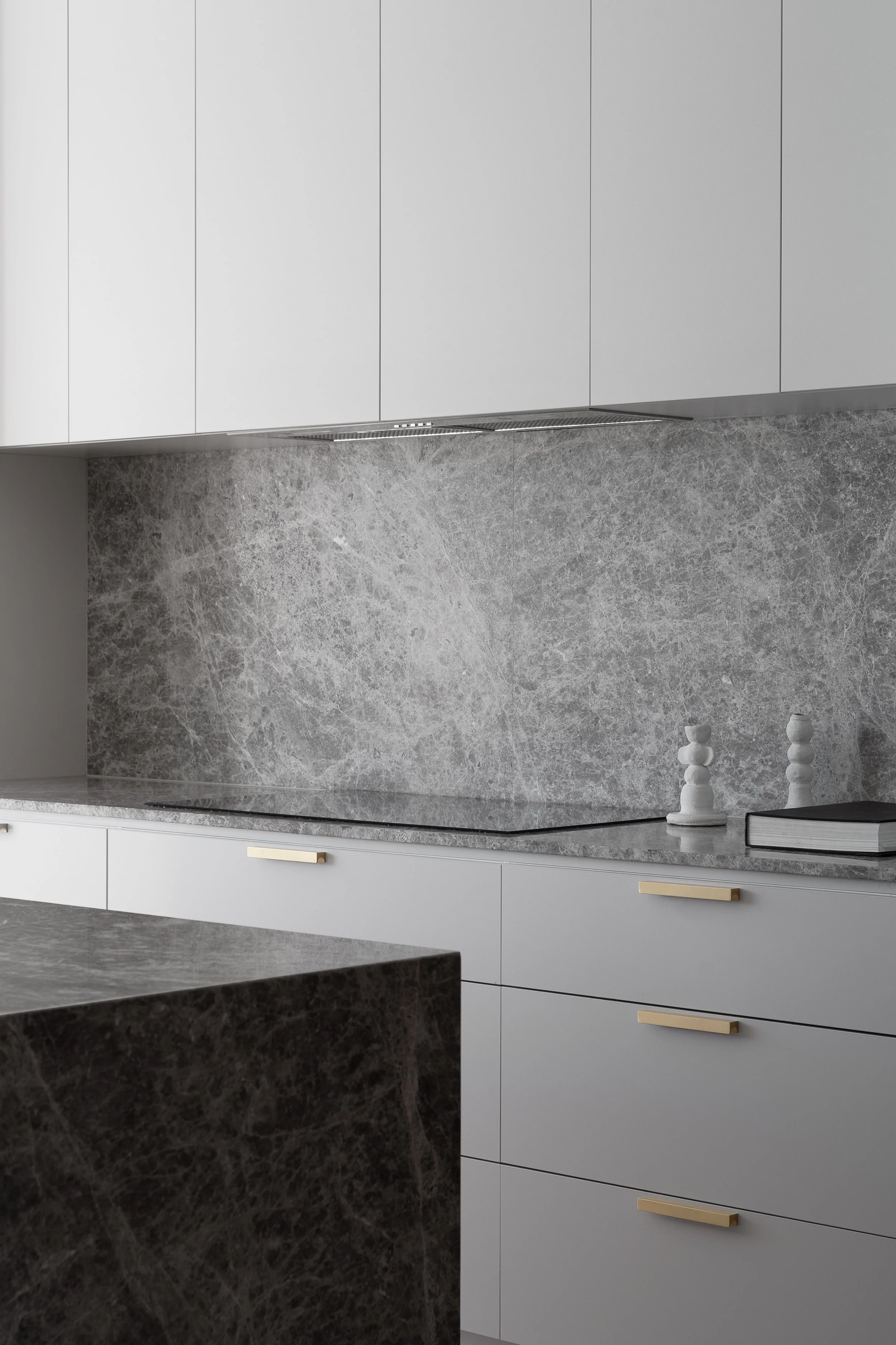 Stone kitchen splashback and cooktop beneath pale cabinetry in Glynde