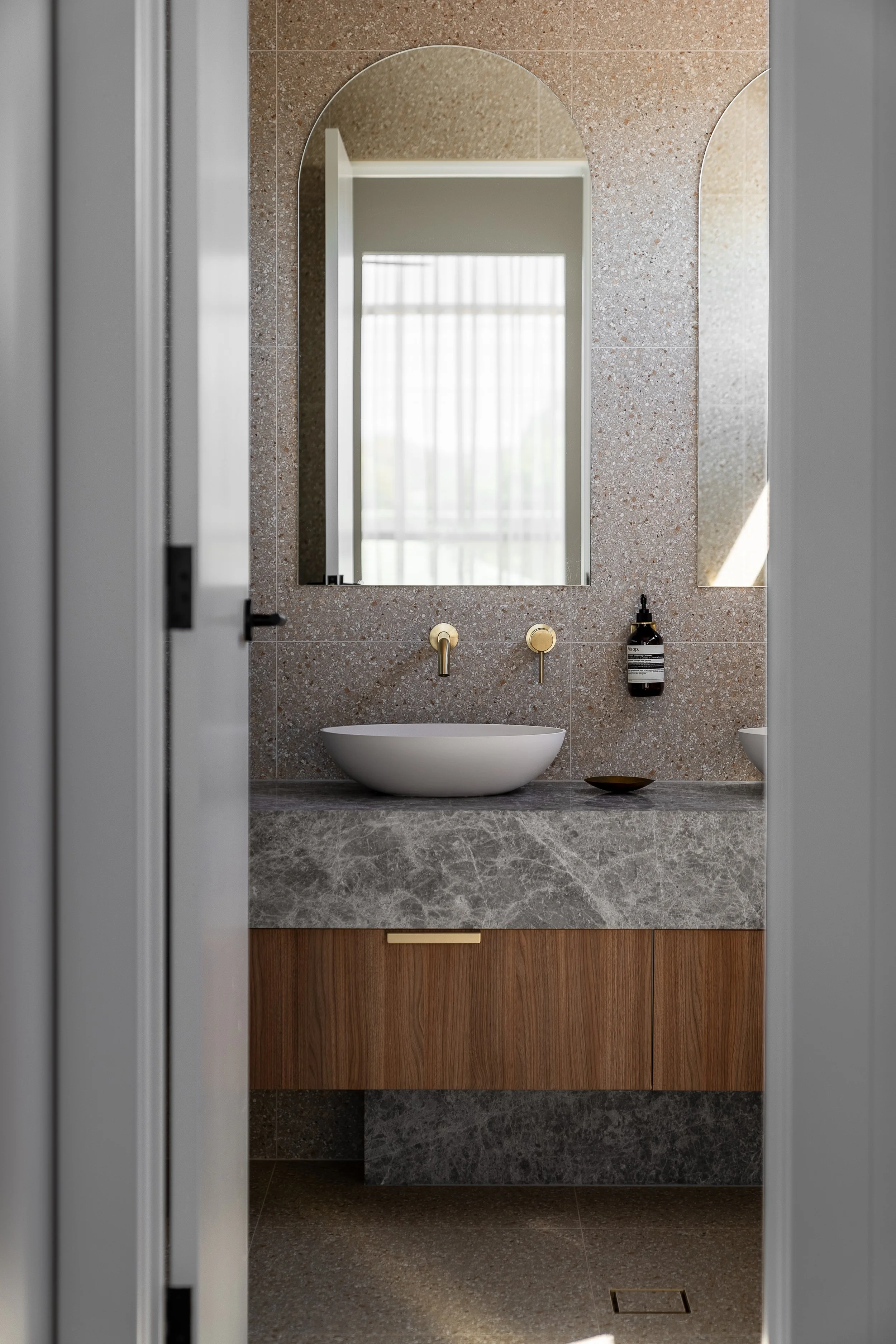 Timber bathroom vanity with a vessel basin and arched mirrors in Glynde