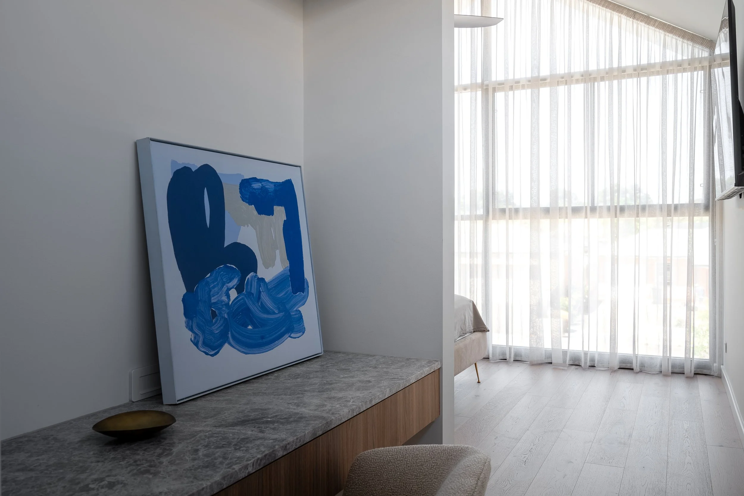 Blue artwork above a timber console beside a sunlit window in Glynde
