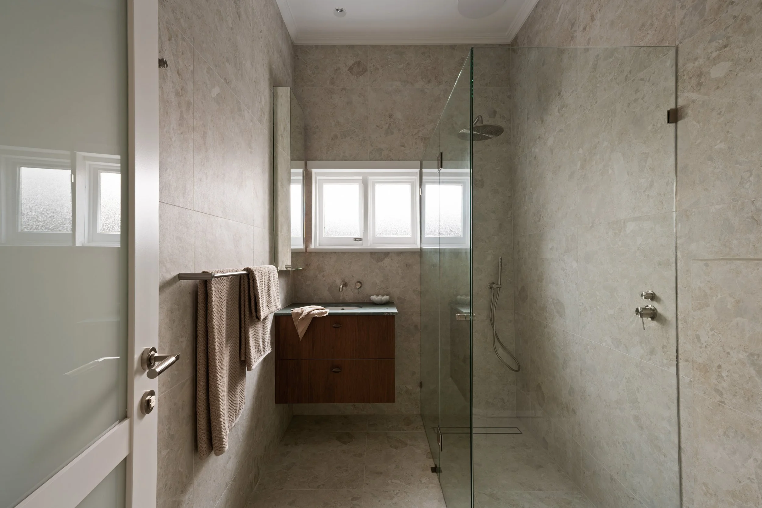 Stone-tiled Glenelg North bathroom with a timber vanity and glass shower