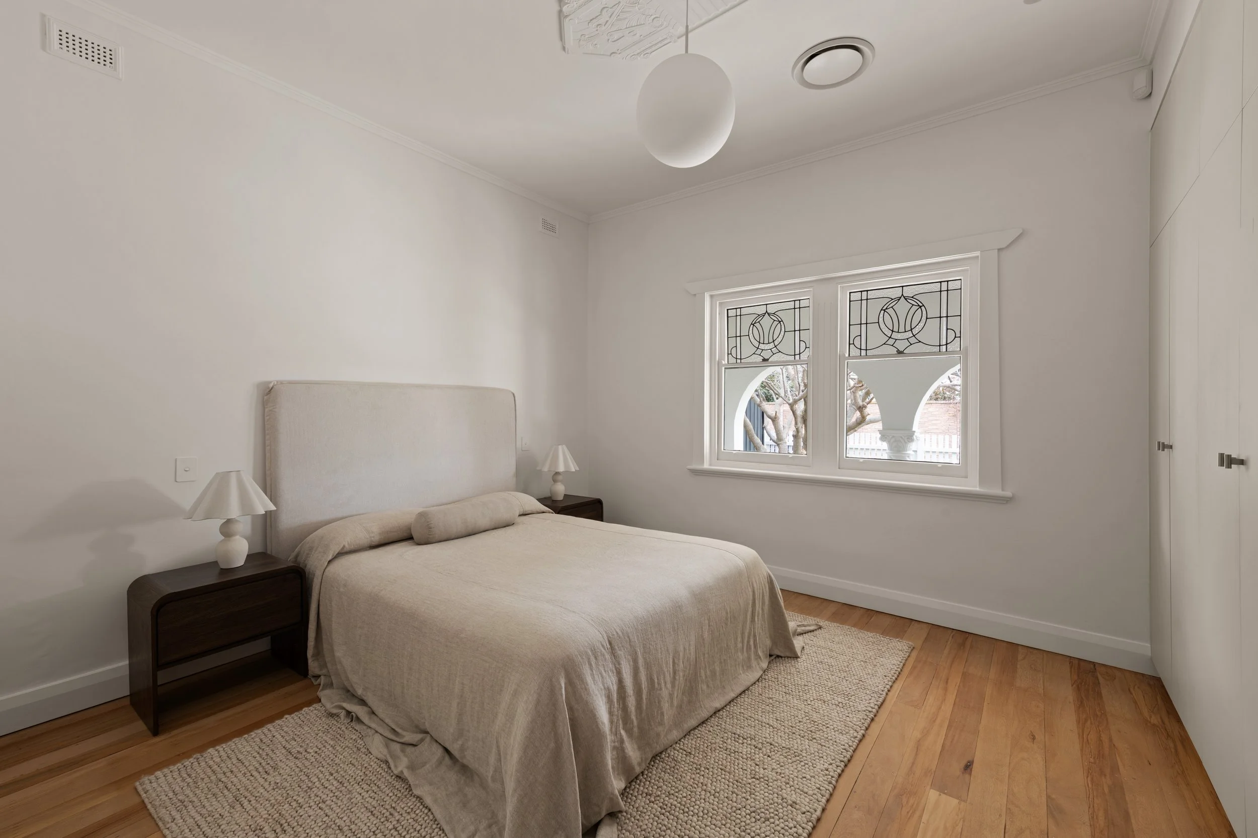 Glenelg North bedroom with timber flooring, white bedding and leadlight windows