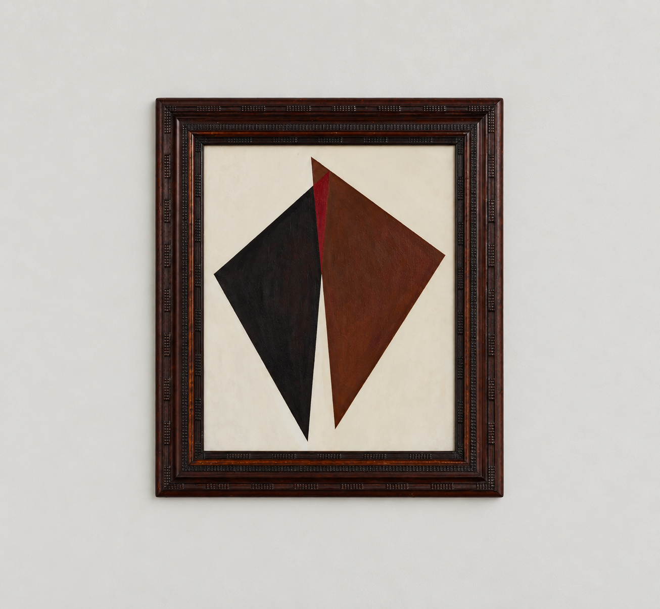 Abstract geometric painting with black, red, and brown shapes in an ornate wooden frame hung on a plain white wall.