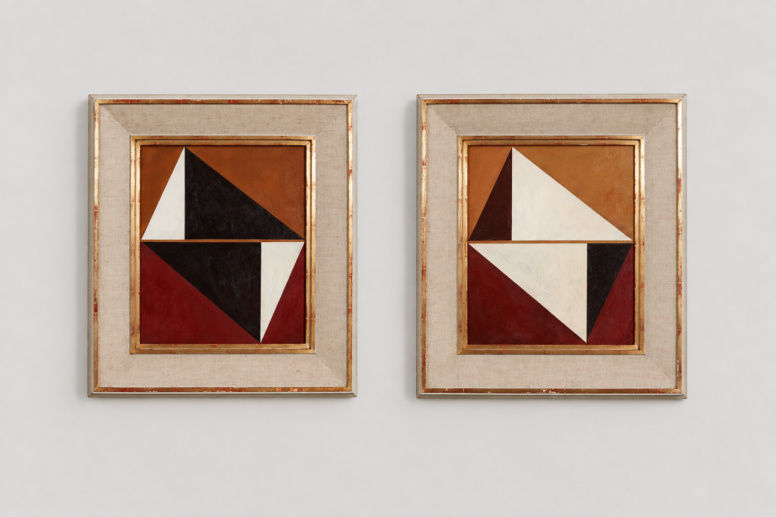 Two framed abstract geometric paintings with triangles and rectangles in red, black, white, and brown tones, hanging on a light-colored wall.