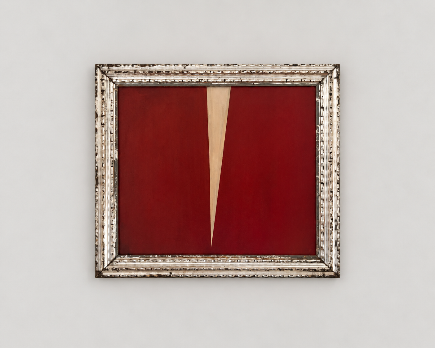 Abstract painting with red background and a large beige V-shaped element, framed in ornate silver frame, hung on a plain white wall.