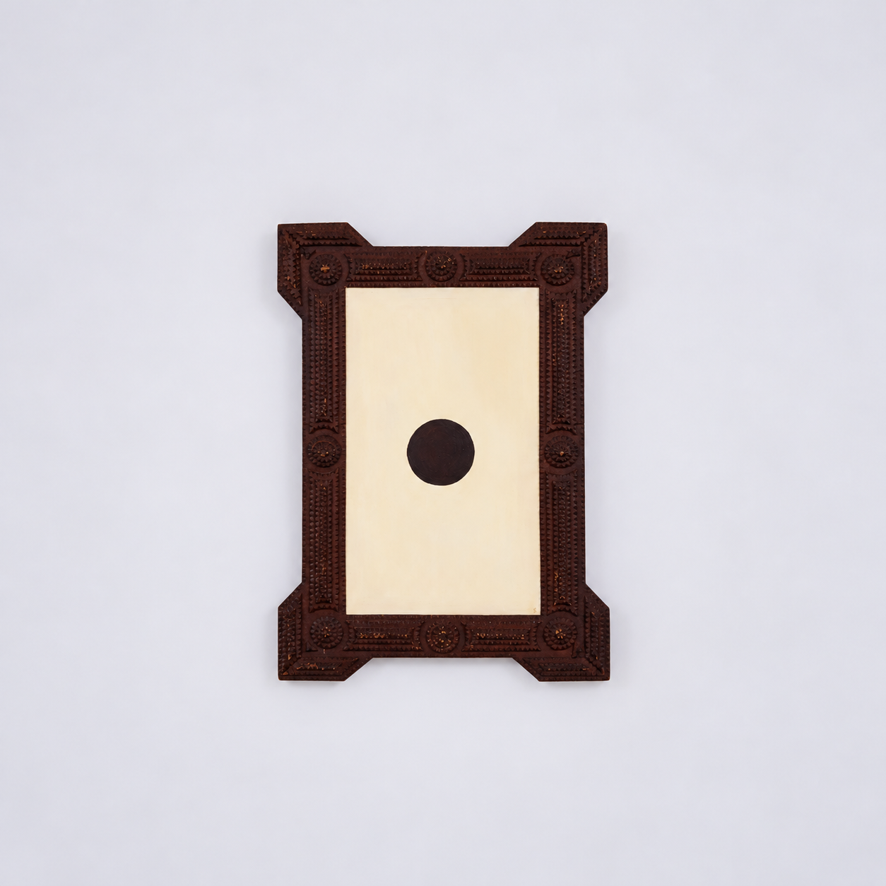 Decorative wooden mirror frame with a black circle in the center, mounted on a plain white wall.