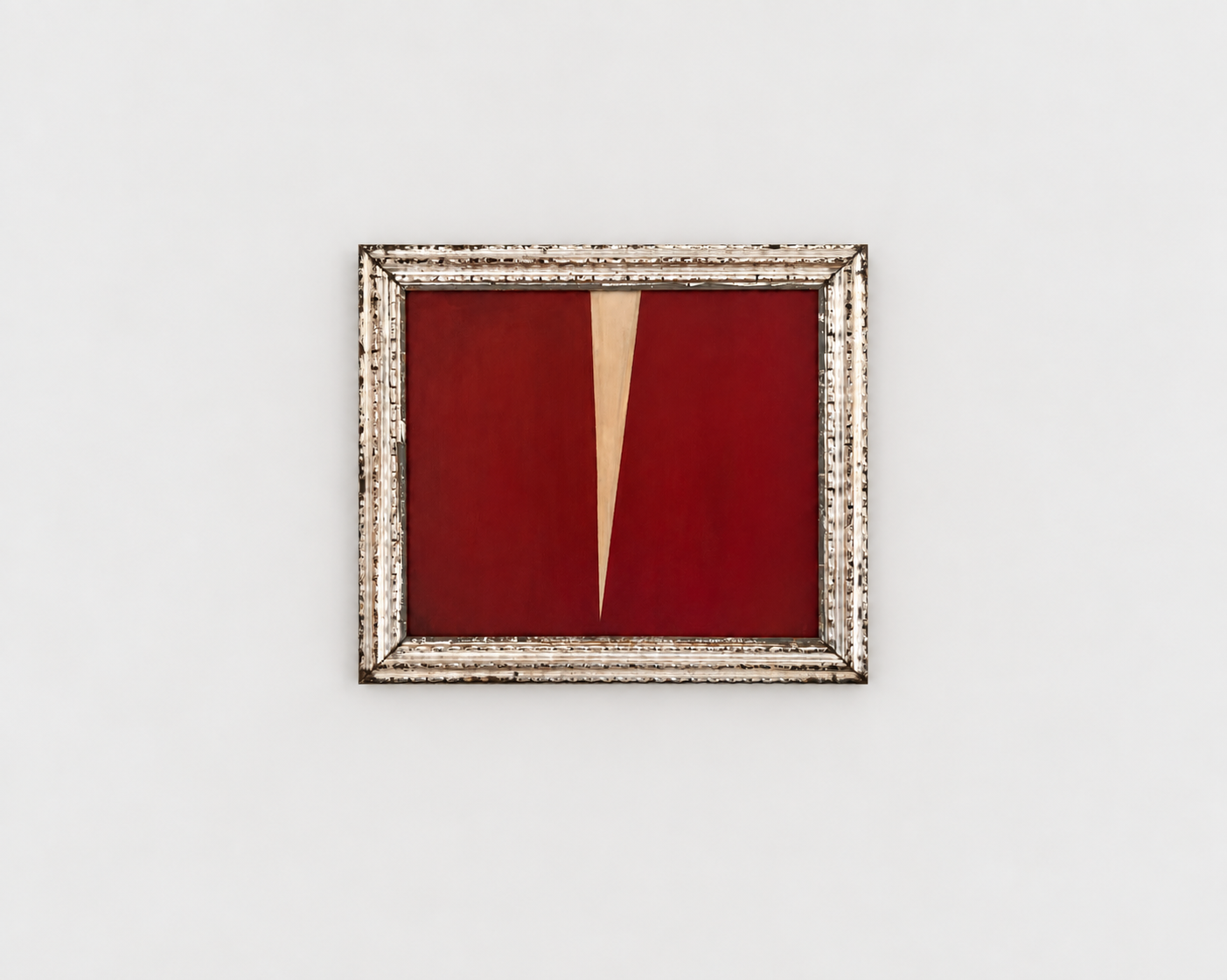 An abstract painting with a bold red background and a central beige triangular shape, framed in a decorative silver frame, hung on a white wall.