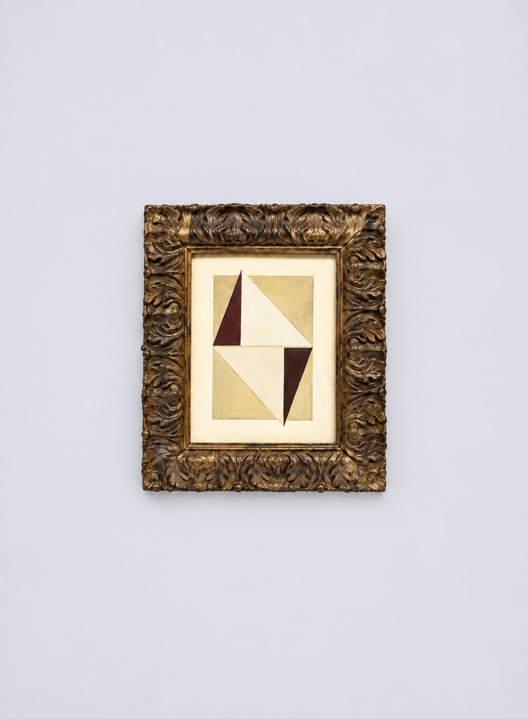 Abstract geometric painting with triangles in shades of brown, beige, and cream, framed with ornate carved wood, hanging on a plain white wall.
