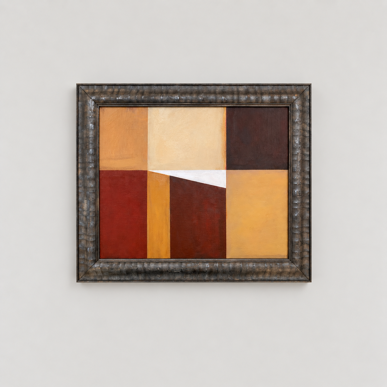 Abstract geometric painting with blocks of orange, yellow, brown, and red, framed in a textured metal frame, hanging on a white wall.