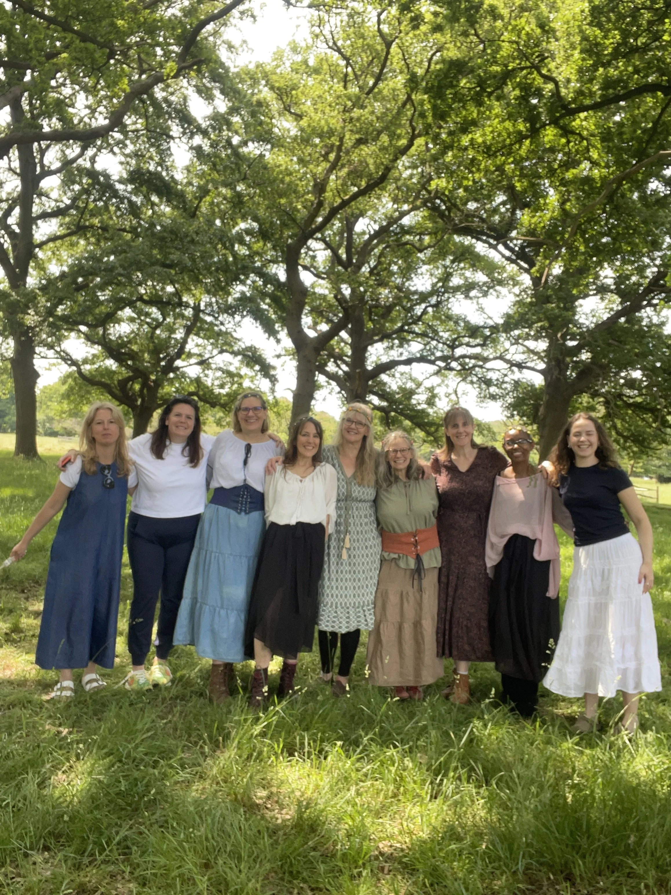 A group of ten women standing outdoors in a park with lush green trees and grass, smiling and posing for a photo.