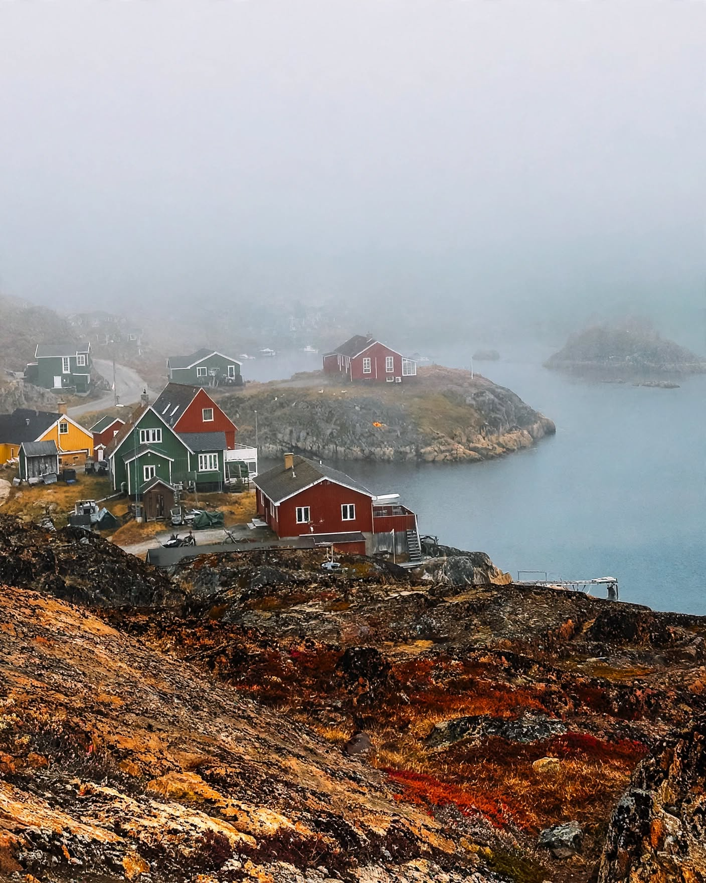 Colorful houses on rocky coast with foggy sky and water in background.