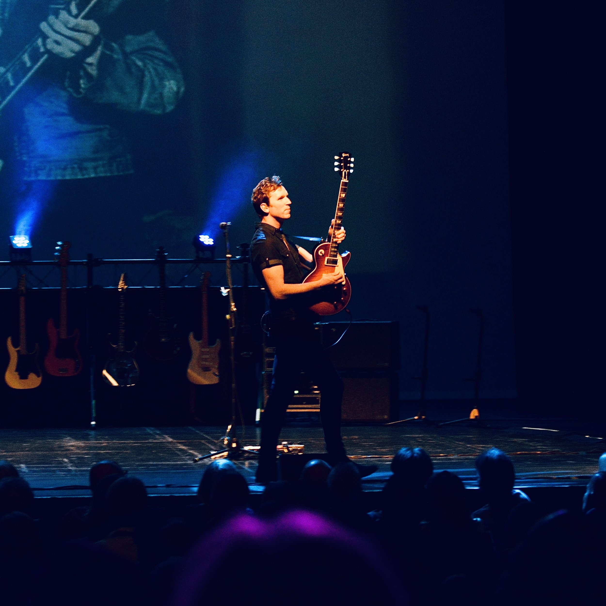 Chris Anthony performing guitar on stage with Story of Guitar Heroes