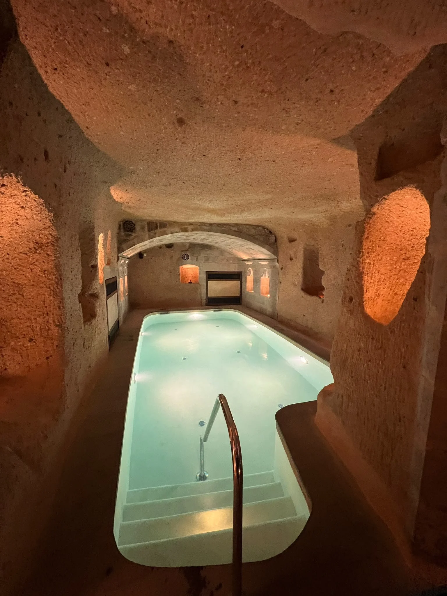 Innenansicht eines geheizten Schwimmbads in einer Höhlengestaltung mit warmem Licht an den Wänden.