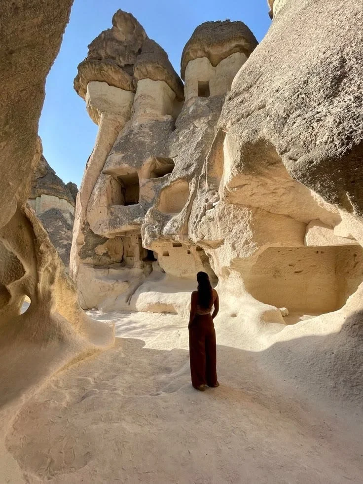 Eine Frau blickt auf eine Felsenlandschaft mit natürlichen Höhlen und Türmen aus Stein, vermutlich in Kappadokien, Türkei, bei Sonnenschein.