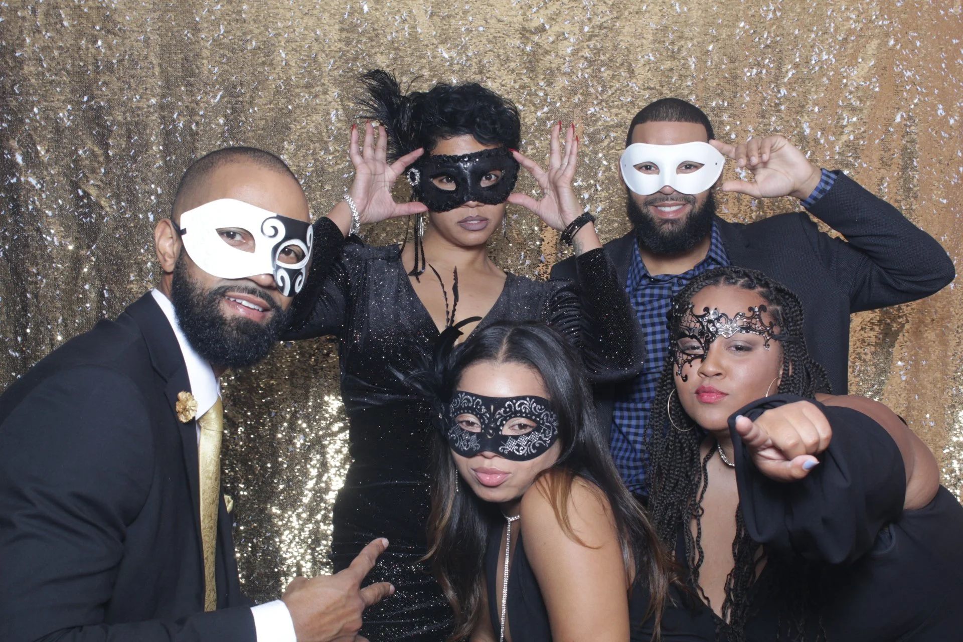Group of six diverse people wearing masks and elegant clothing, posing for photo against a gold, sparkly backdrop.