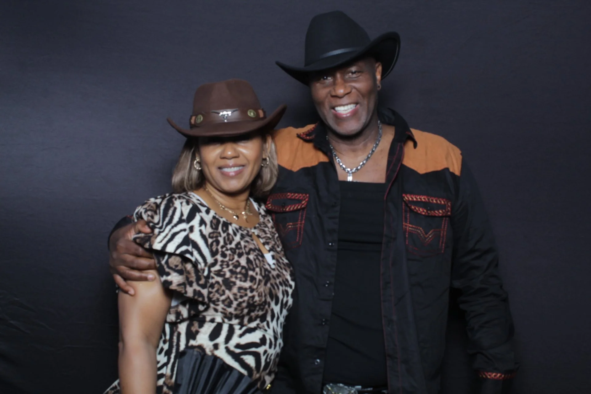 Two smiling guests in cowboy hats posing together against a dark photo booth backdrop.