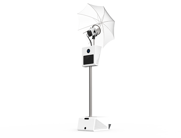 Angled view of the white Legacy Photo Booth with umbrella lighting, camera, touchscreen and print stand.