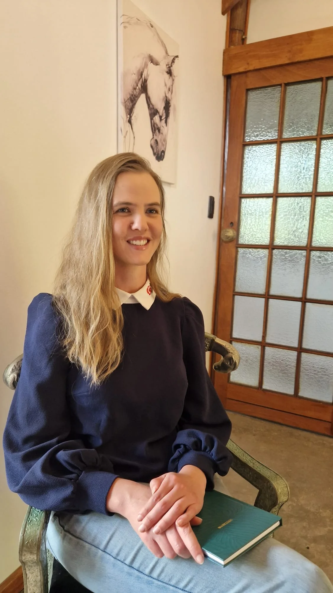 Portrait of Cyan Jolliffe, Specialist Wellness Counsellor, seated with a book in a welcoming space.