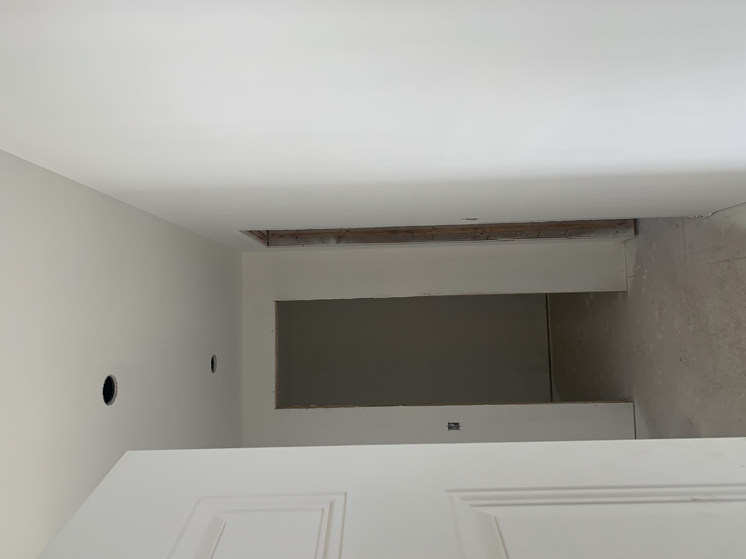 Unfinished hallway with white walls, open doorways, and a concrete floor, under construction.