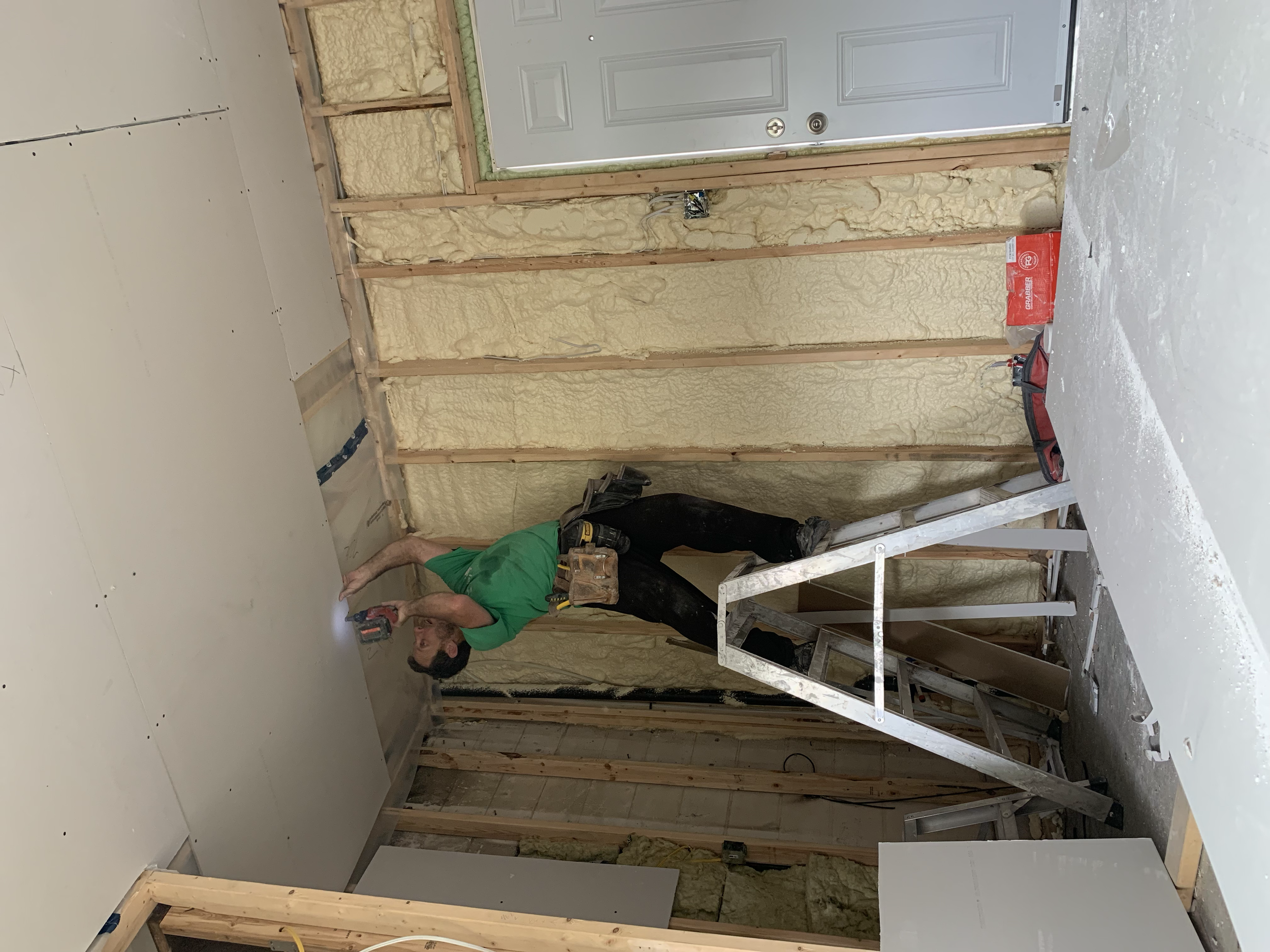 A man standing on a step ladder installing drywall on a ceiling in an unfinished room.