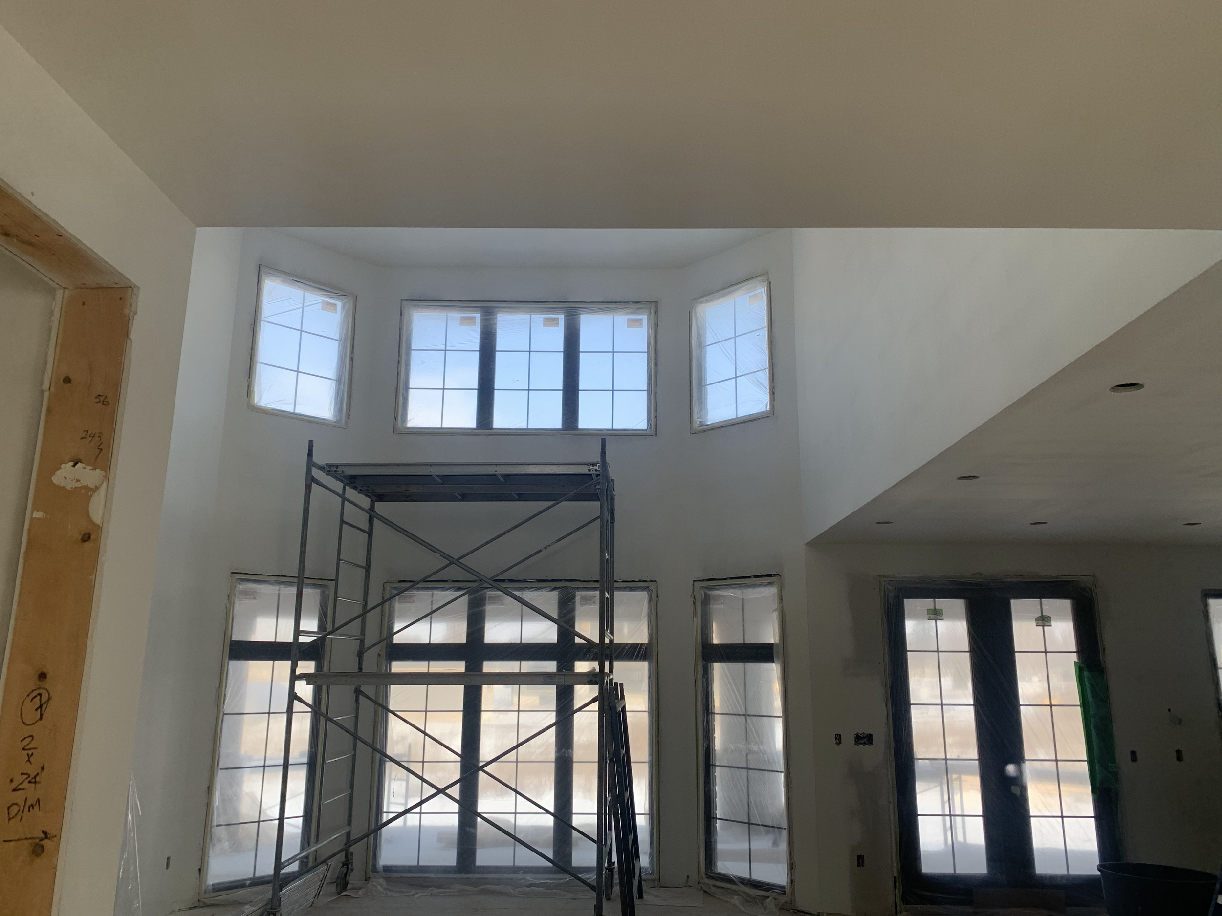 Interior under construction with large windows, scaffolding, and unfinished walls.