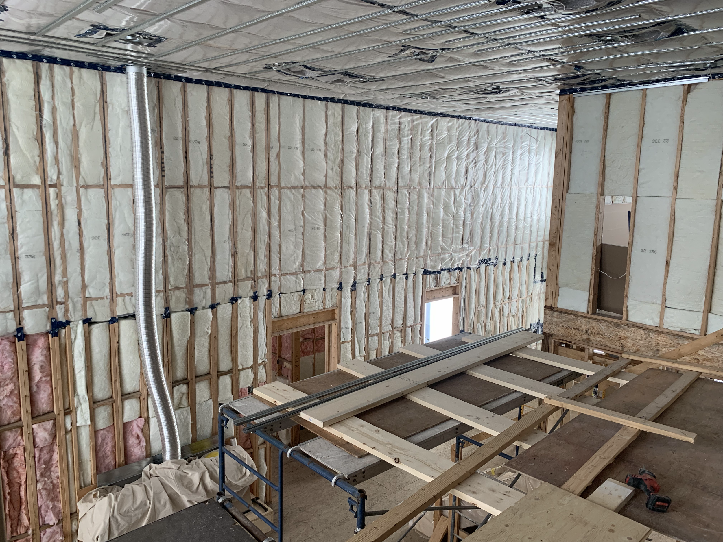 Interior view of a building under construction, showing wooden framework, insulation, metal ductwork, and exposed ceiling.