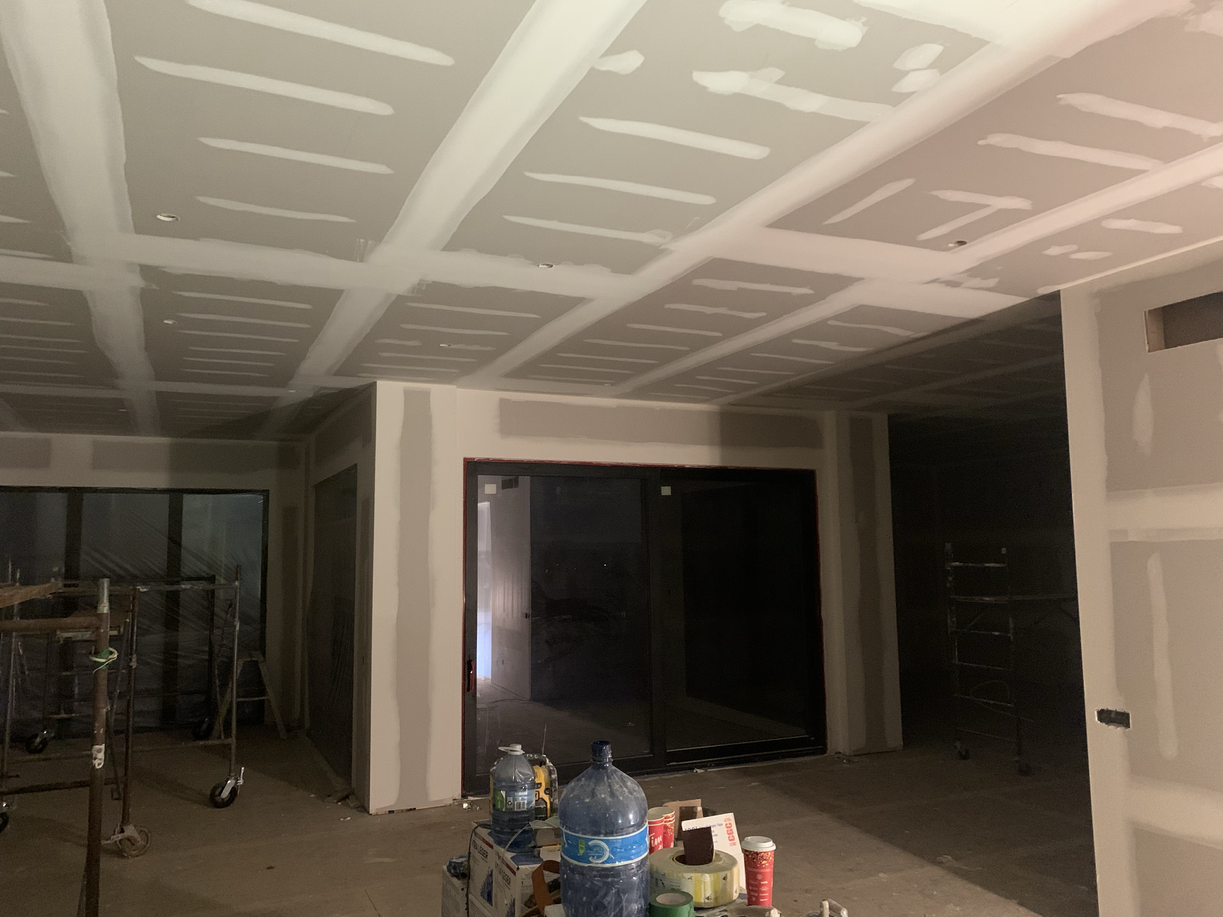 Interior room under construction with drywall ceiling partially finished, construction tools and equipment on the floor.