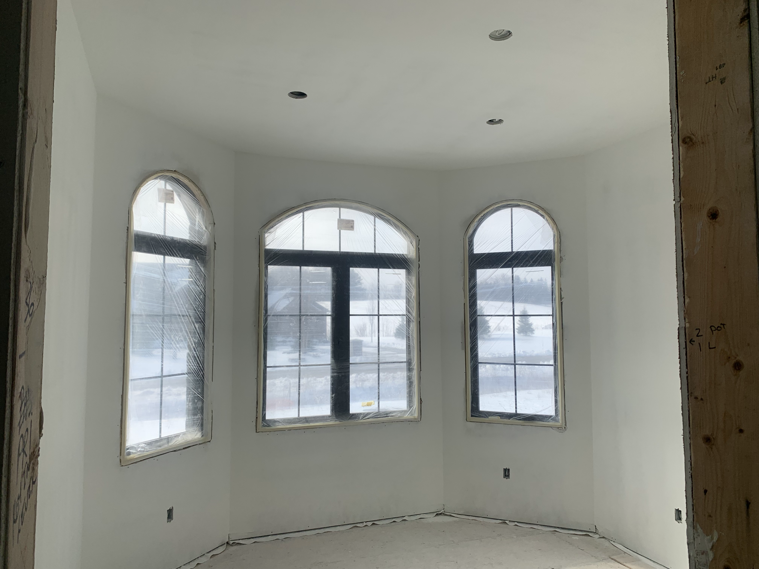 Under construction interior room with three large windows and recessed lighting in the ceiling, with visible framing and construction notes on the walls.