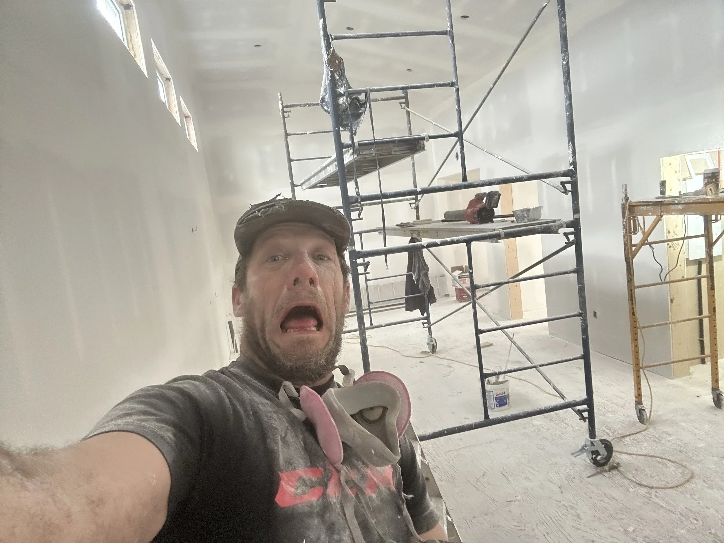 A man taking a selfie in a room under construction with scaffolding and construction tools visible in the background.