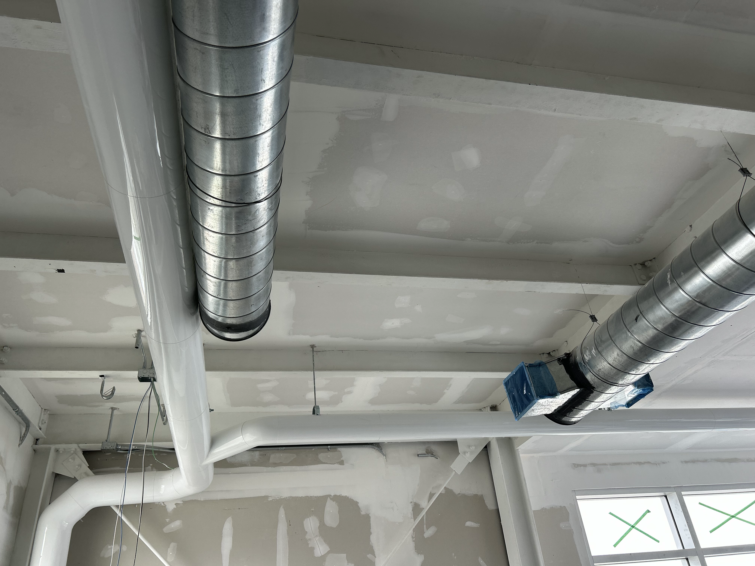 Construction site ceiling with ductwork, pipes, and electrical wiring, and drywall in progress.