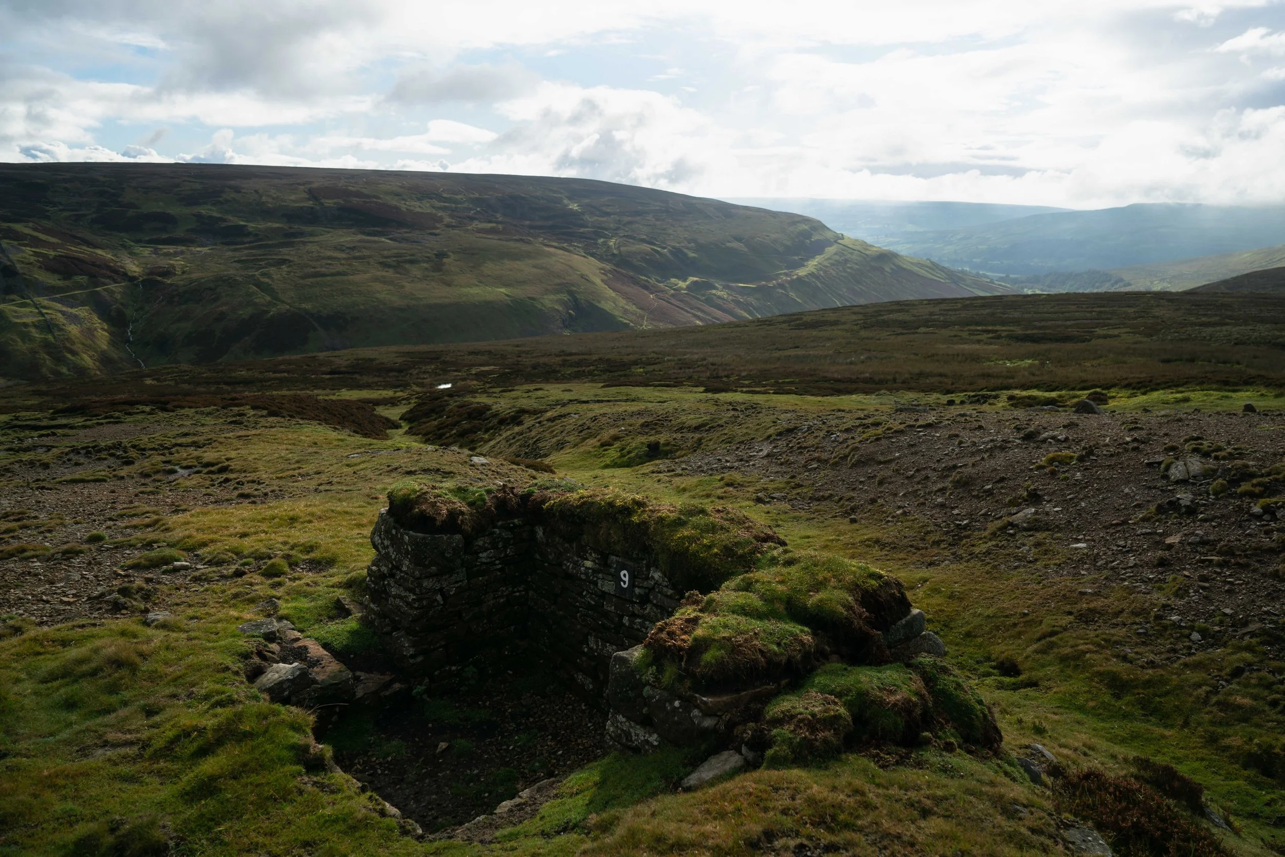 A landscape of rolling green hills and mountains with cloudy sky.