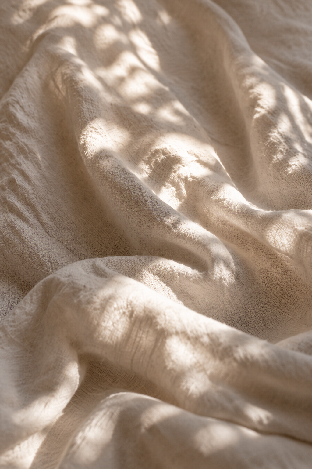 Close-up of soft, light-colored fabric with natural sunlight and shadows creating a textured, wrinkled appearance.