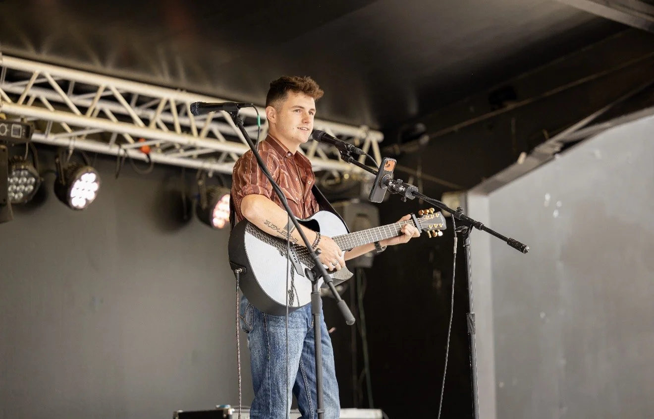 Young man performing on stage with an acoustic guitar, microphone, and stage lighting