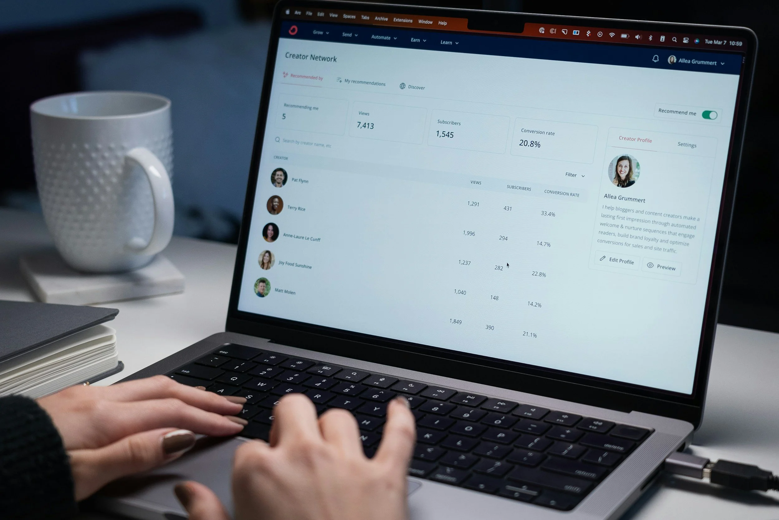 A person typing on a laptop keyboard with a mug on a napkin holder nearby, displaying a social media creator analytics dashboard on the screen.