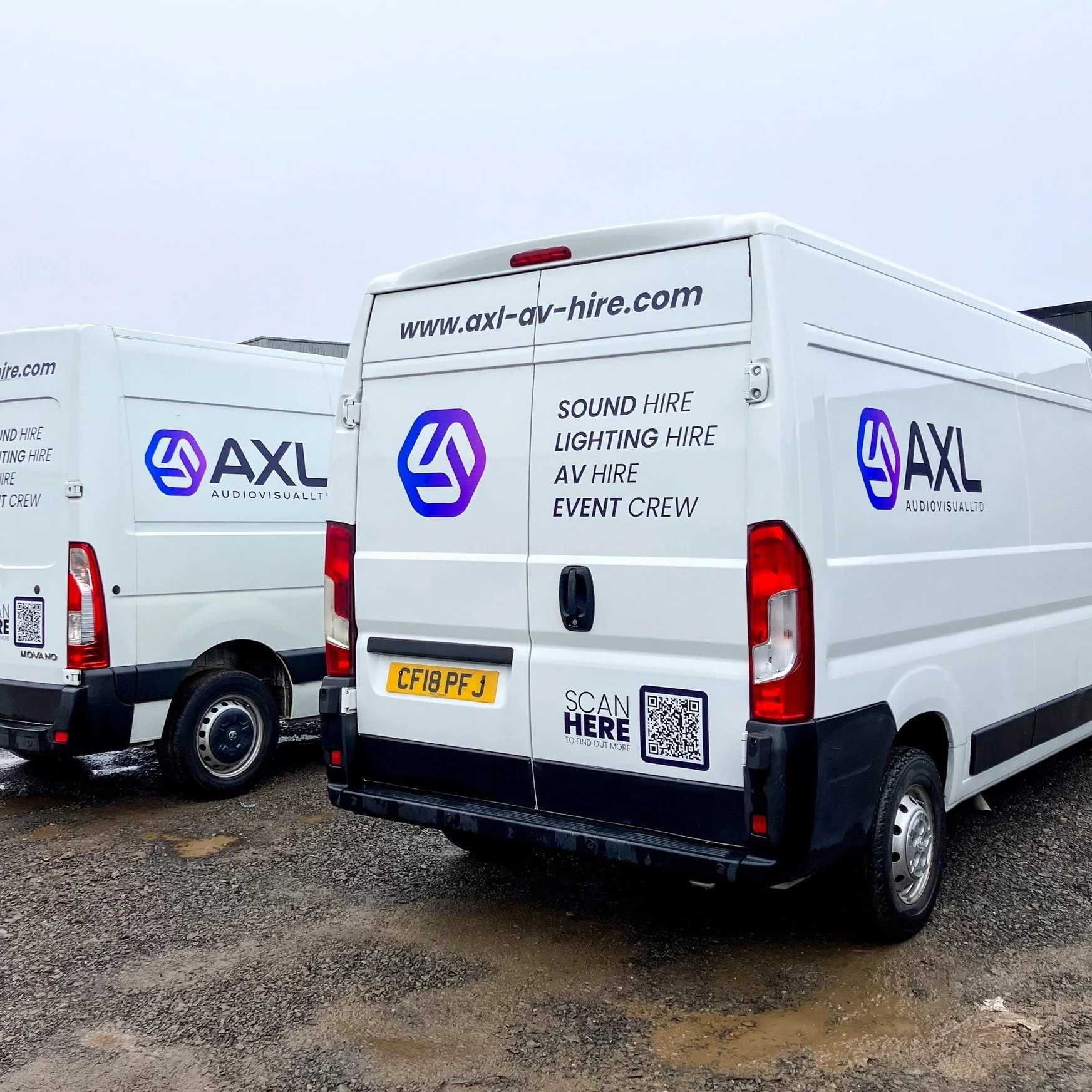 Two white service vans parked on a gravel lot, with the logo and contact information for AXL Audiovisual on the back of each vehicle.