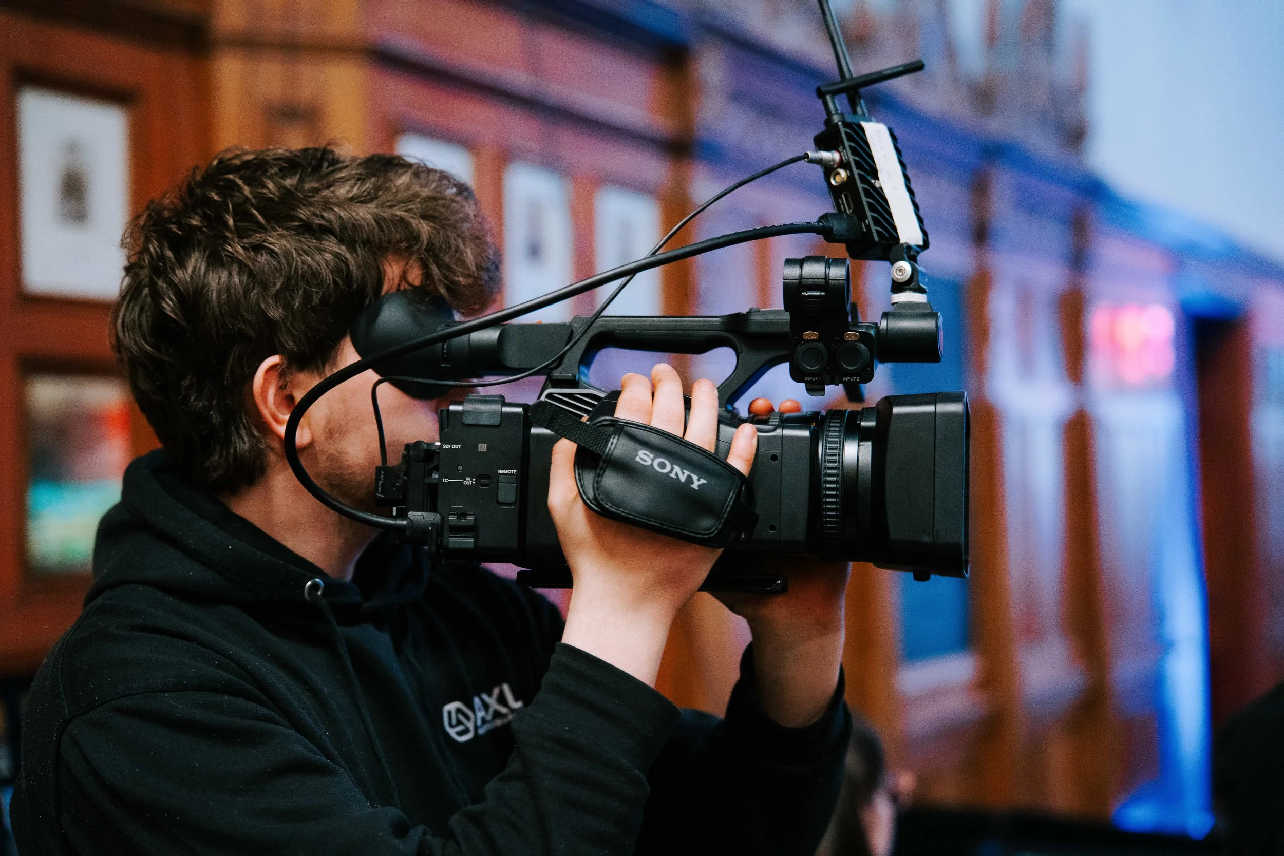 AXL camera operator filming a corporate event on a shoulder-mounted Sony camcorder