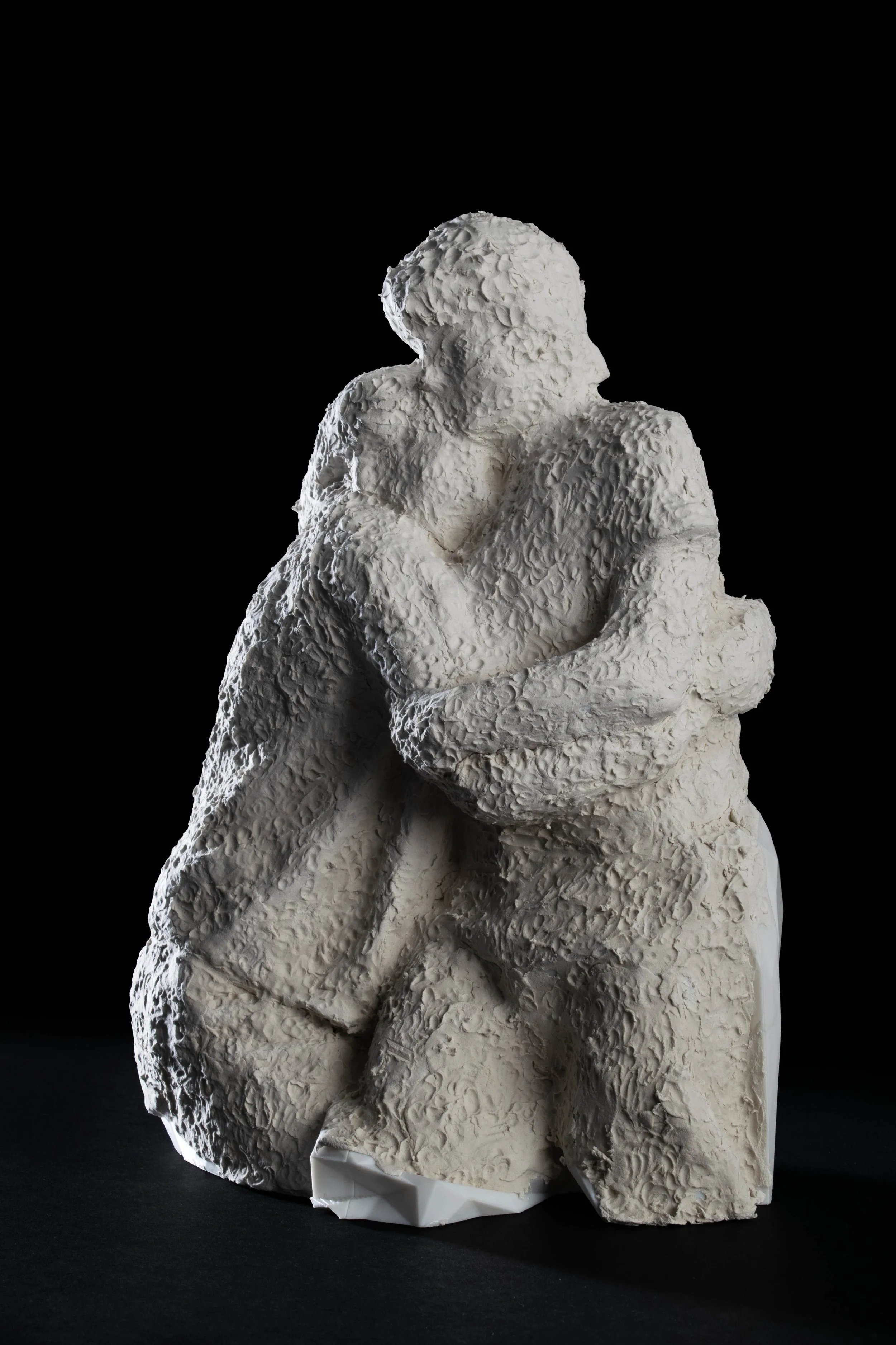 White sculptural art piece of a person with crossed arms, sitting and looking to the side, set against a black background.