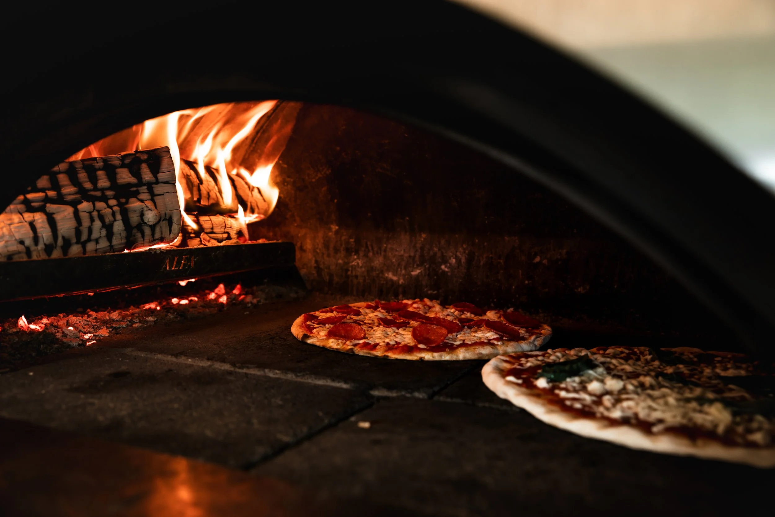 Pizza baking inside a wood-fired oven with glowing flames
