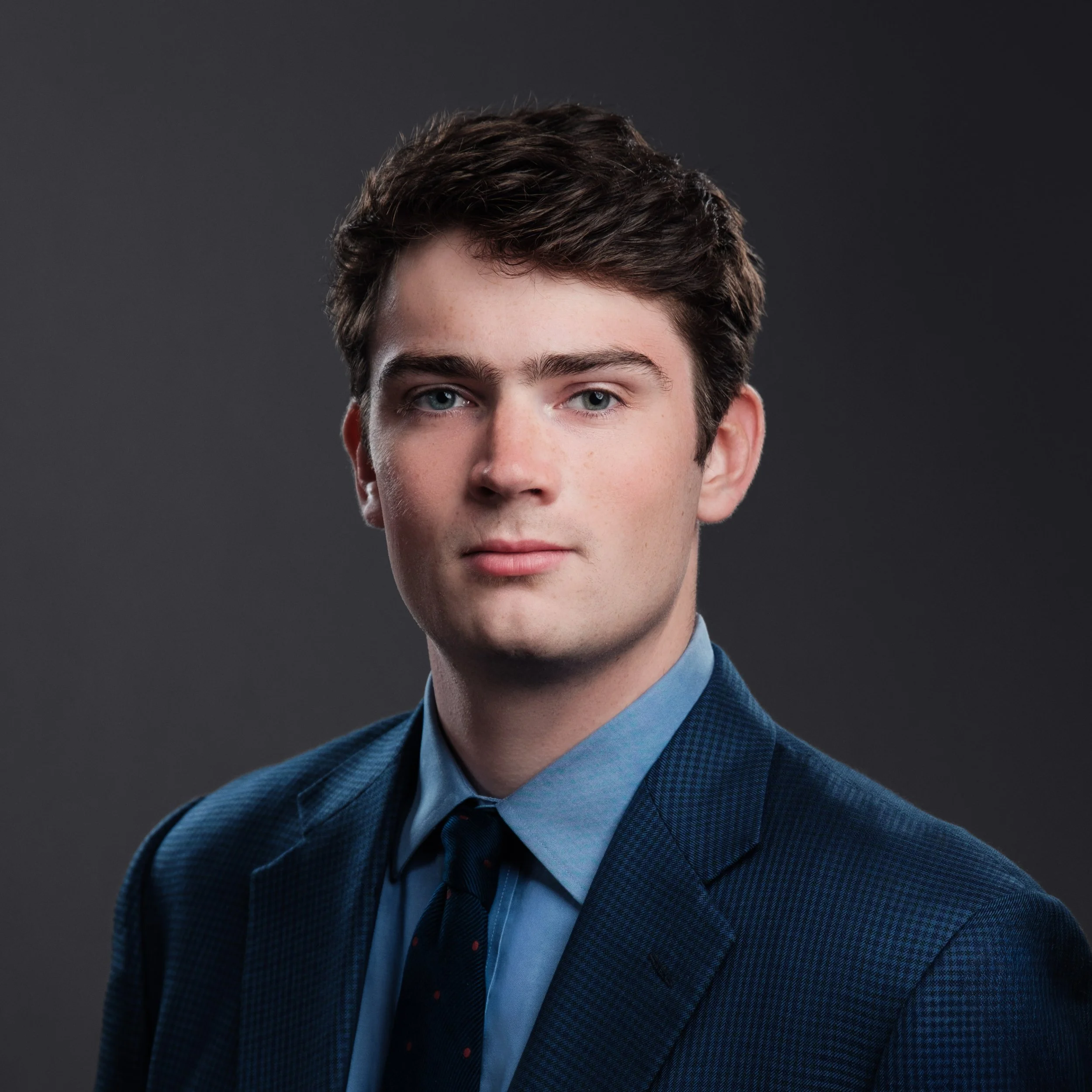 Male finance executive wearing a navy blue suit jacket, light blue dress shirt and dark tie for his headshot session