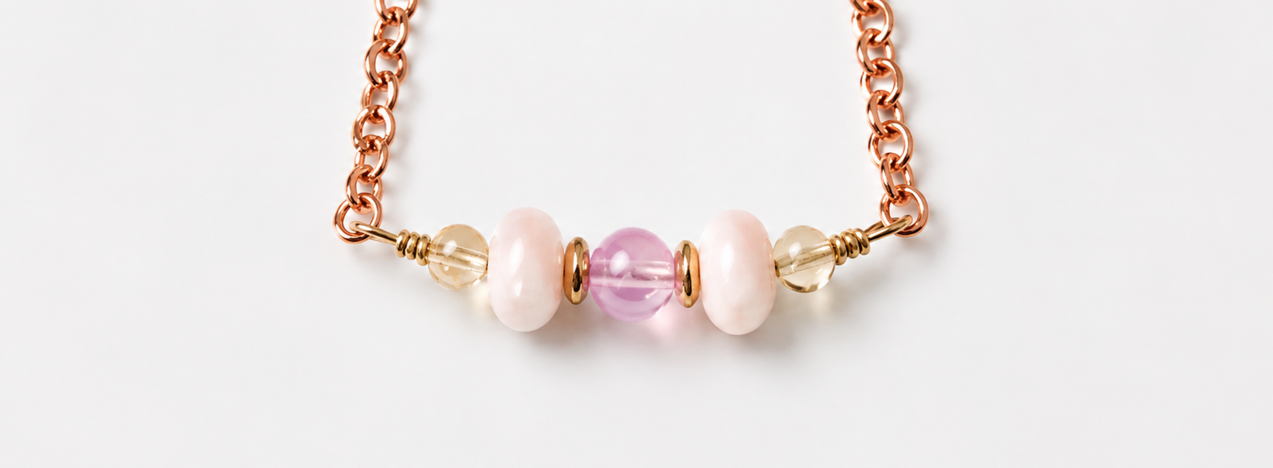 A close-up of a necklace with pink, cream, and translucent beads on a rose gold chain, against a white background.