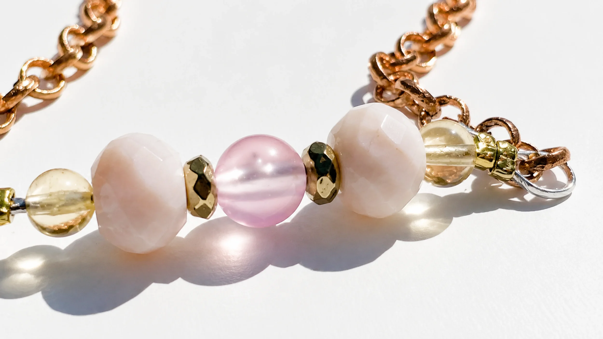 Close-up of a beaded bracelet with pink, ivory, and gold beads on a white surface, casting shadows.