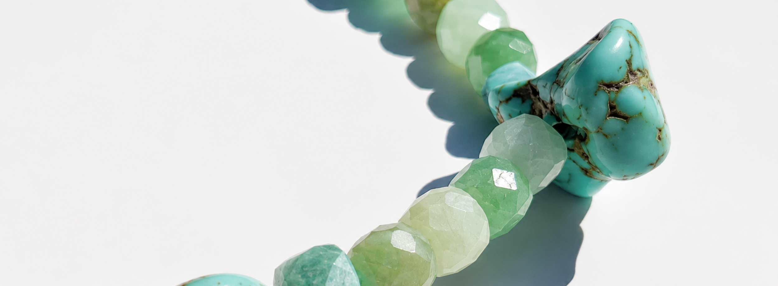 A close-up of a strand of pastel-colored beads, featuring turquoise, light green, yellow, and clear faceted stones, with a large turquoise stone with black veins attached.