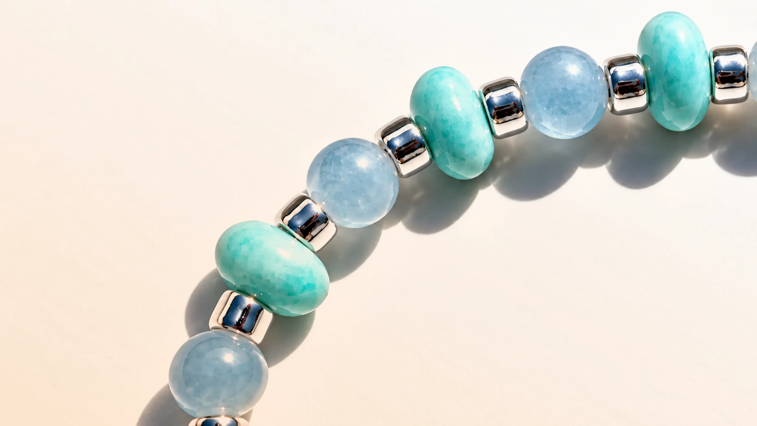 A beaded bracelet with alternating turquoise and blue beads, separated by shiny silver spacer beads, arranged in a semi-circle on a neutral background.