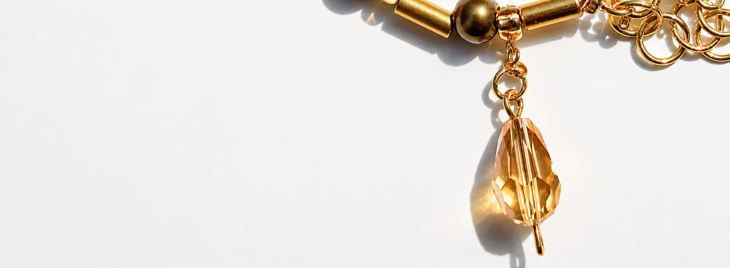 Close-up of a gold and beaded necklace with a large, faceted, peach-colored gemstone pendant on a white background.