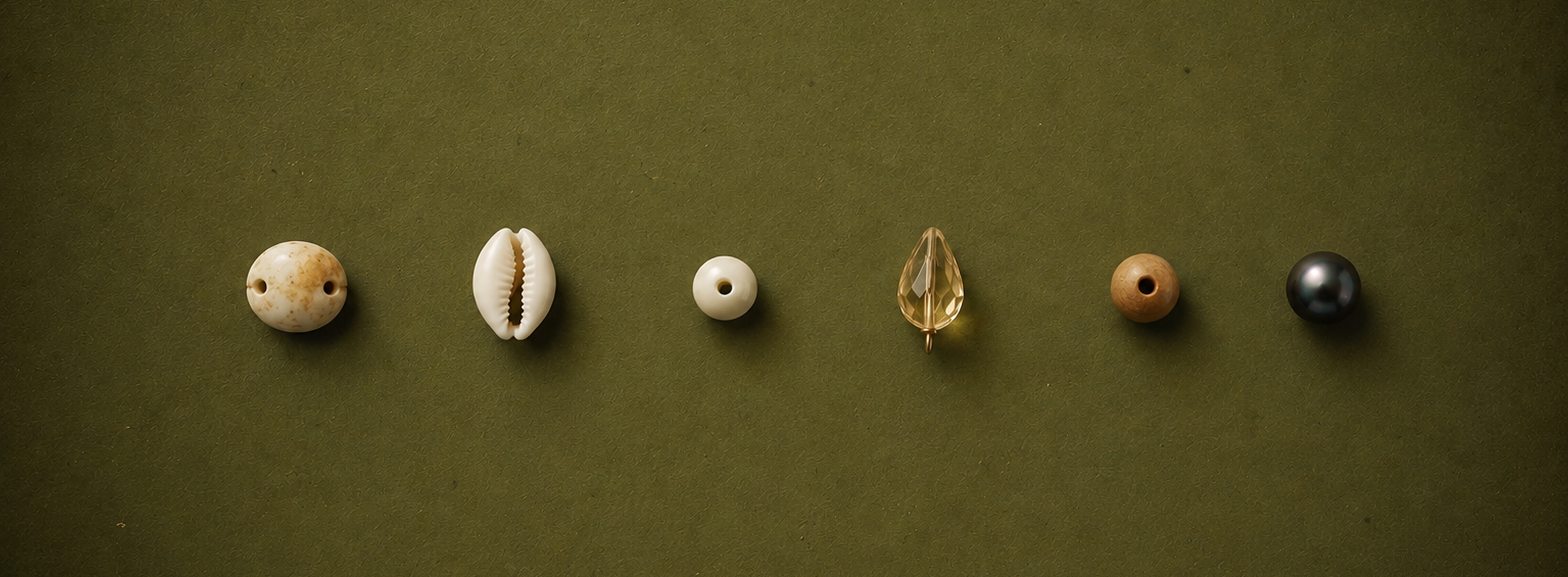 A row of seven decorative beads on a green background, including a spotted round bead, a shell-shaped bead, a small white bead, a faceted drop-shaped bead, a wooden bead, and a metallic bead.