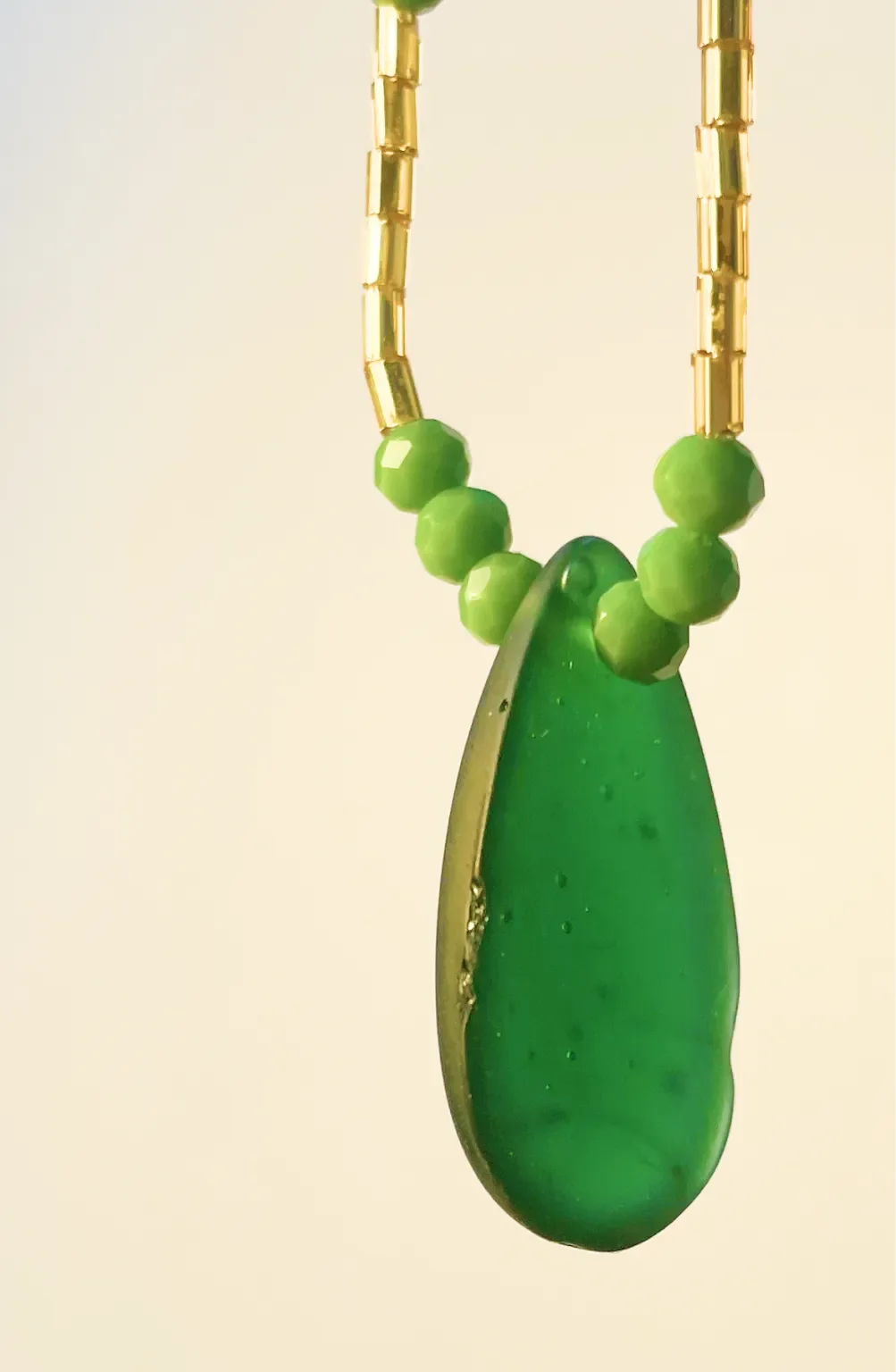 Close-up of a necklace with green beads and a large green pendant, hanging on a gold chain.
