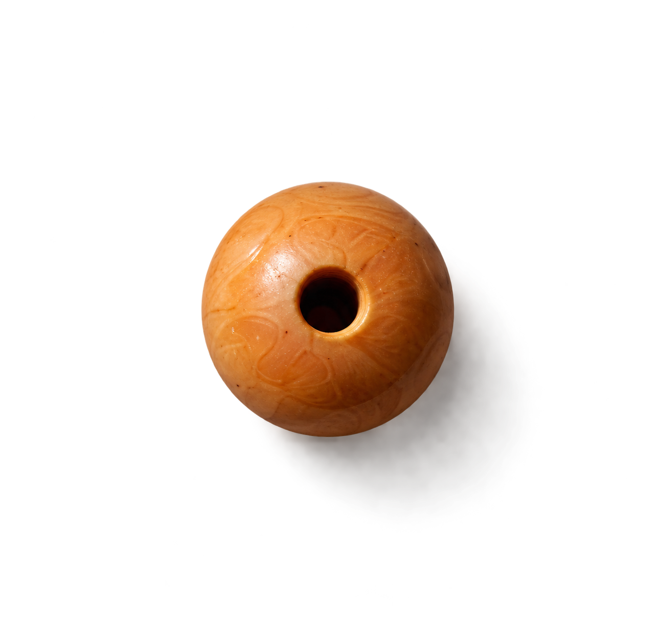 Top view of a round, orange marble with a hole in the center, casting a shadow on a black surface.