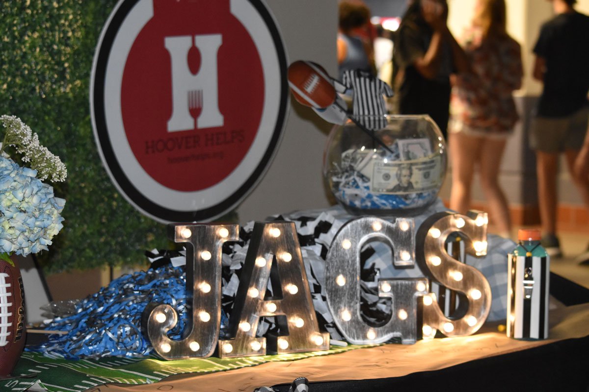Decorative display celebrating a sports event, with illuminated letters spelling 'JAGS', a fish bowl with dollar bills, and crowd in the background.