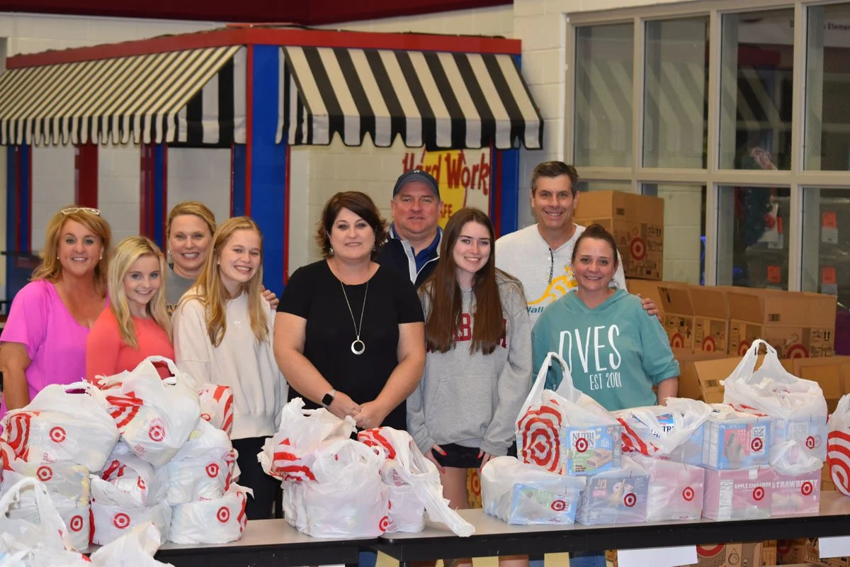 Group of people standing behind tables filled with bags of donated items at a Target charity event.