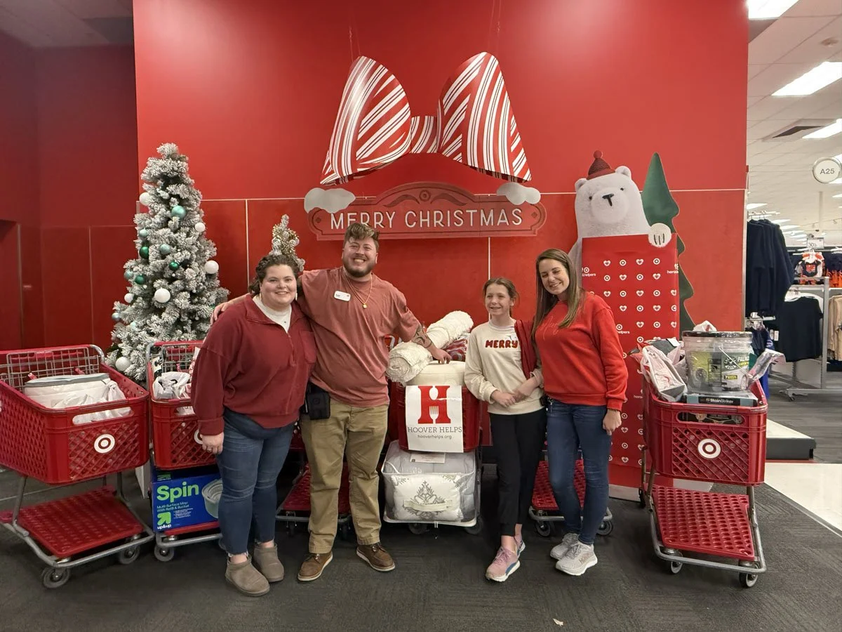 Four people standing in front of a Christmas display at Target, featuring a snow-covered Christmas tree, large bow decoration, and a polar bear holding a Christmas tree, with shopping carts nearby.