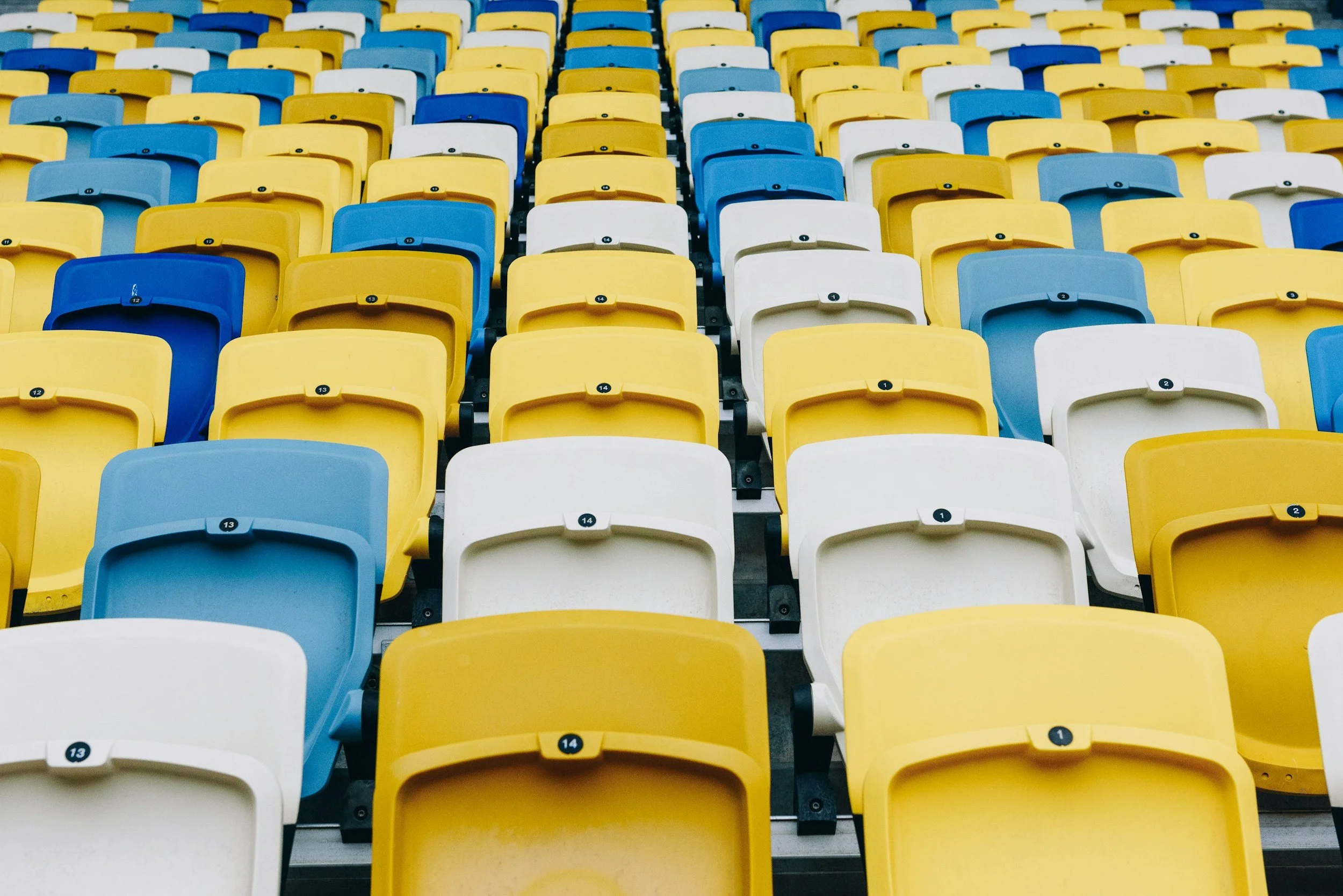Empty stadium seats in yellow, blue, and white colors, arranged in rows.